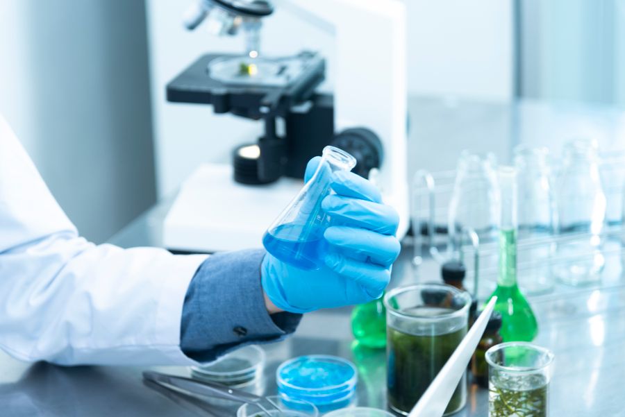 Profissional segurando frasco de análise ao lado de microscópio